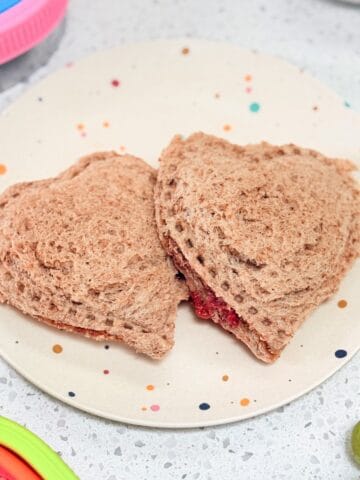 Homemade uncrustable sandwiches in the shape of hearts on polka dot toddler plate.
