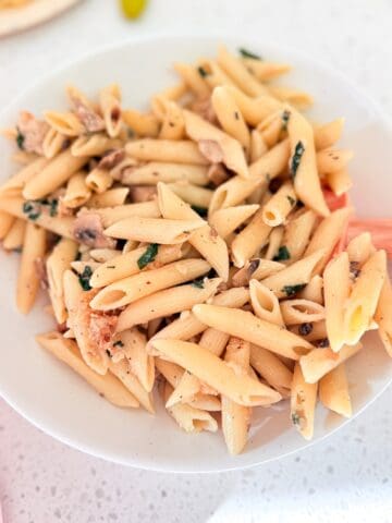 Parmesan chicken pasta served in a white bowl with a wooden spoon on the kitchen counter